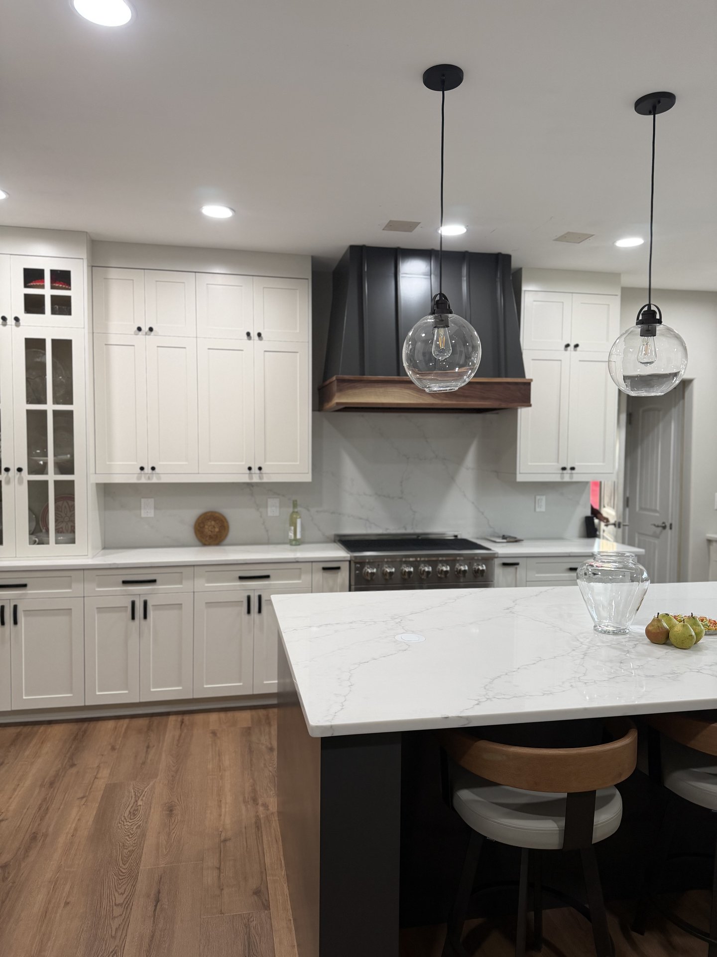 Completed kitchen with white shaker cabinets quartz island and custom range hood by Hatley Construction Clayton NC